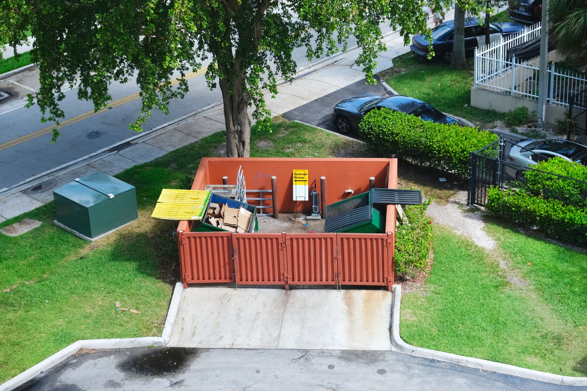 Dumpster half-filled with garbage next to residential area, road and parking lot behind commercial building aerial street view photo. Waste management concept. Dumpster half-filled with garbage next to residential area, road and parking lot behind commercial building aerial street view photo. Waste management concept.
